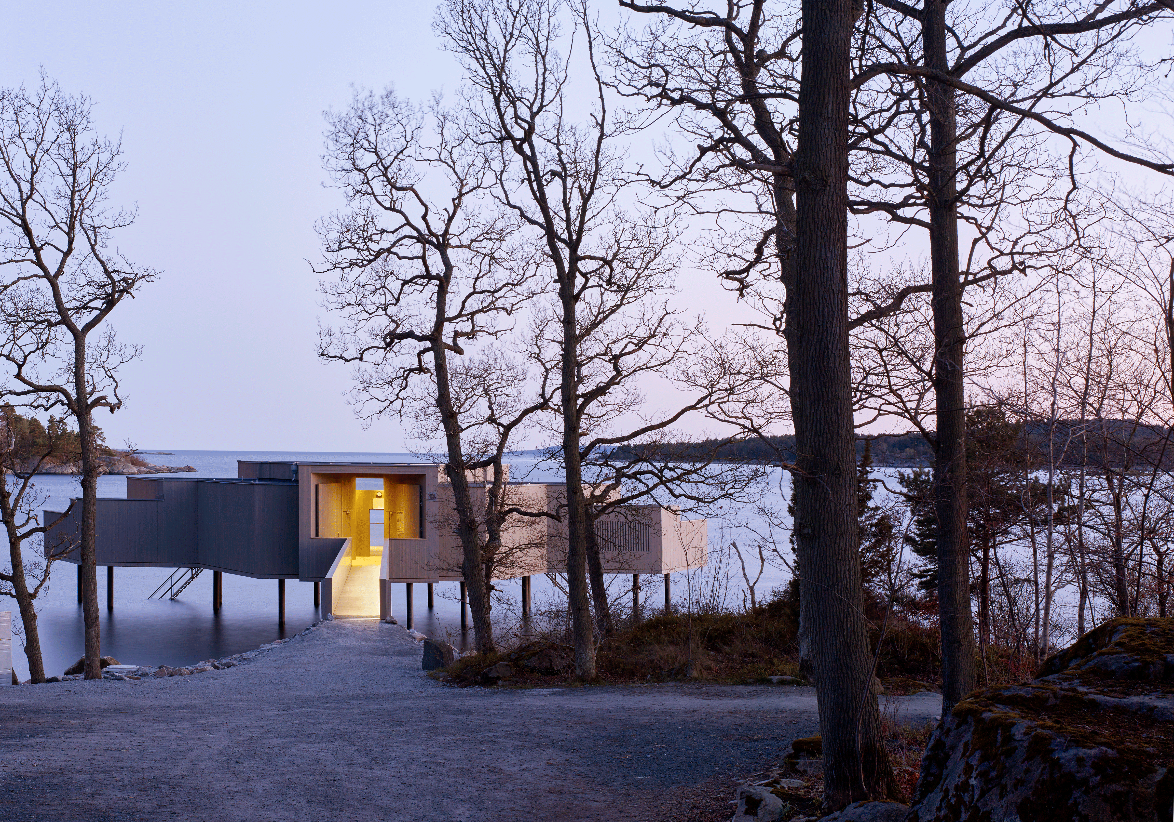 Kallbadhus skymtar bakom vinterkala träd.