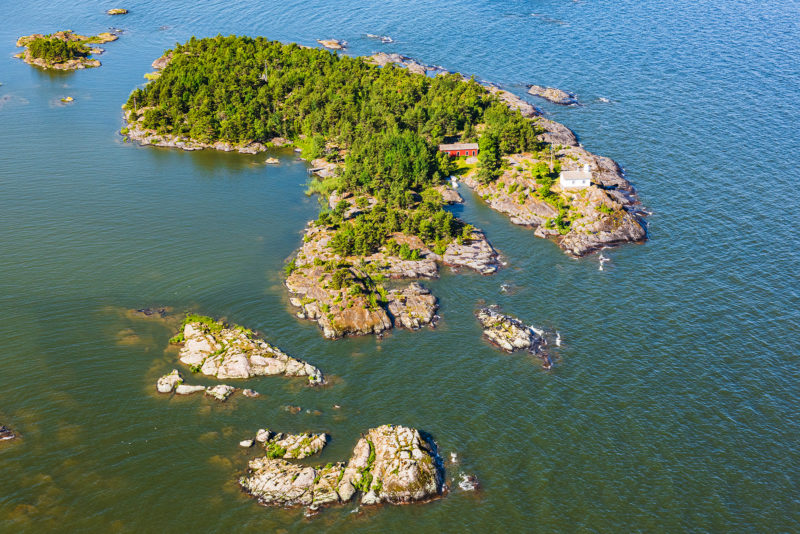 Drönarbild över en skogbeklädd ö omgiven av vatten.