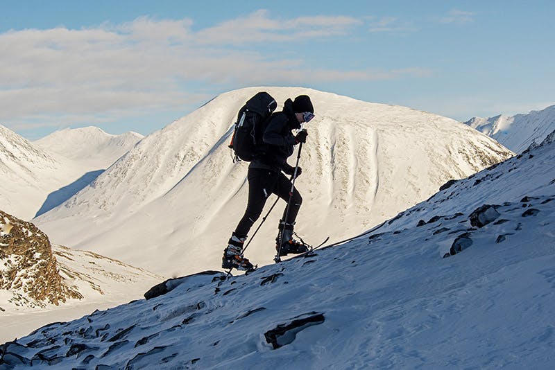 En skidåkare i motljus går uppför ett berg i Kirunafjällen på skidor med stighudar.