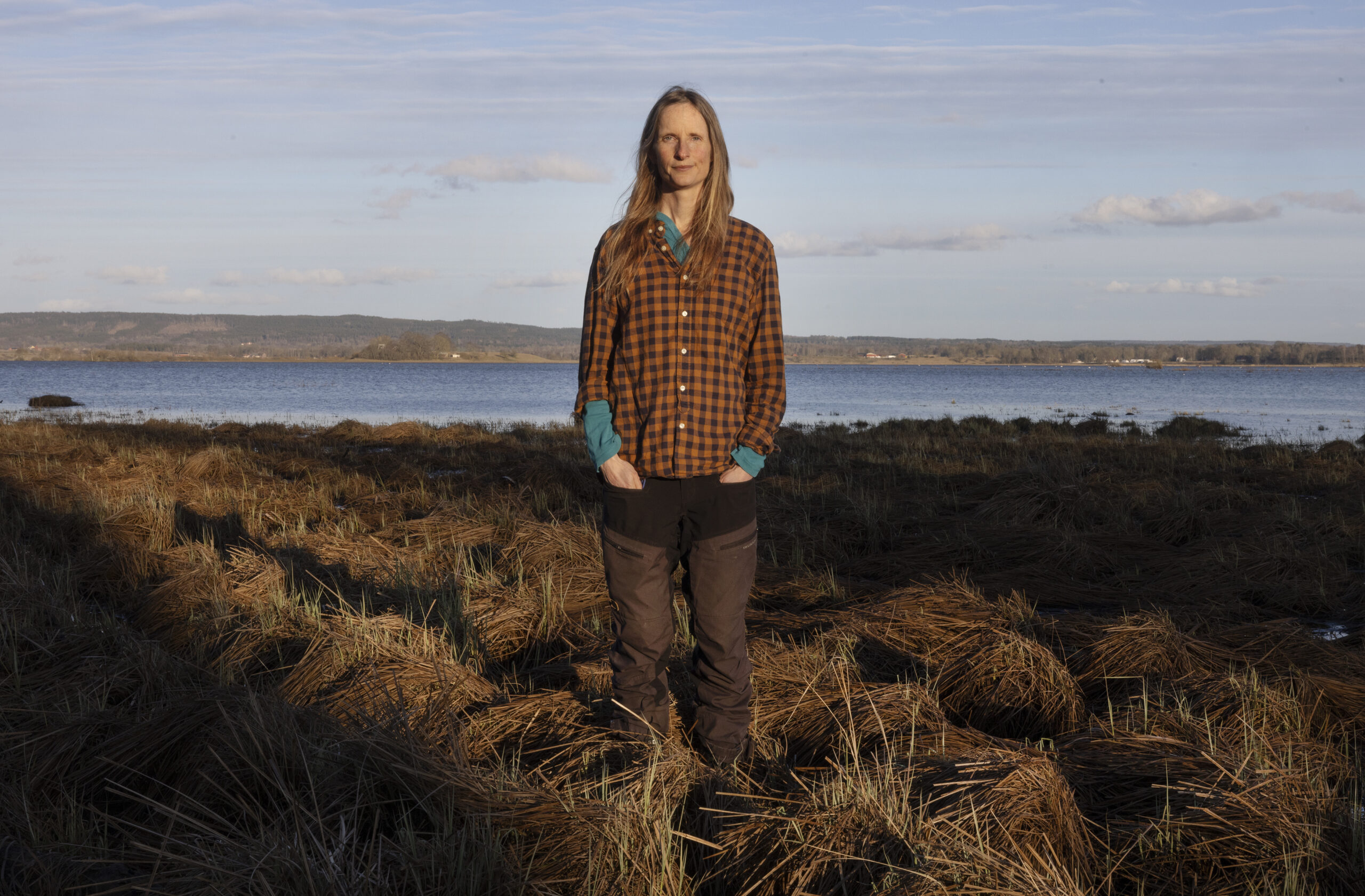 Anna Froster stående på en mosse med vatten i bakgrunden.