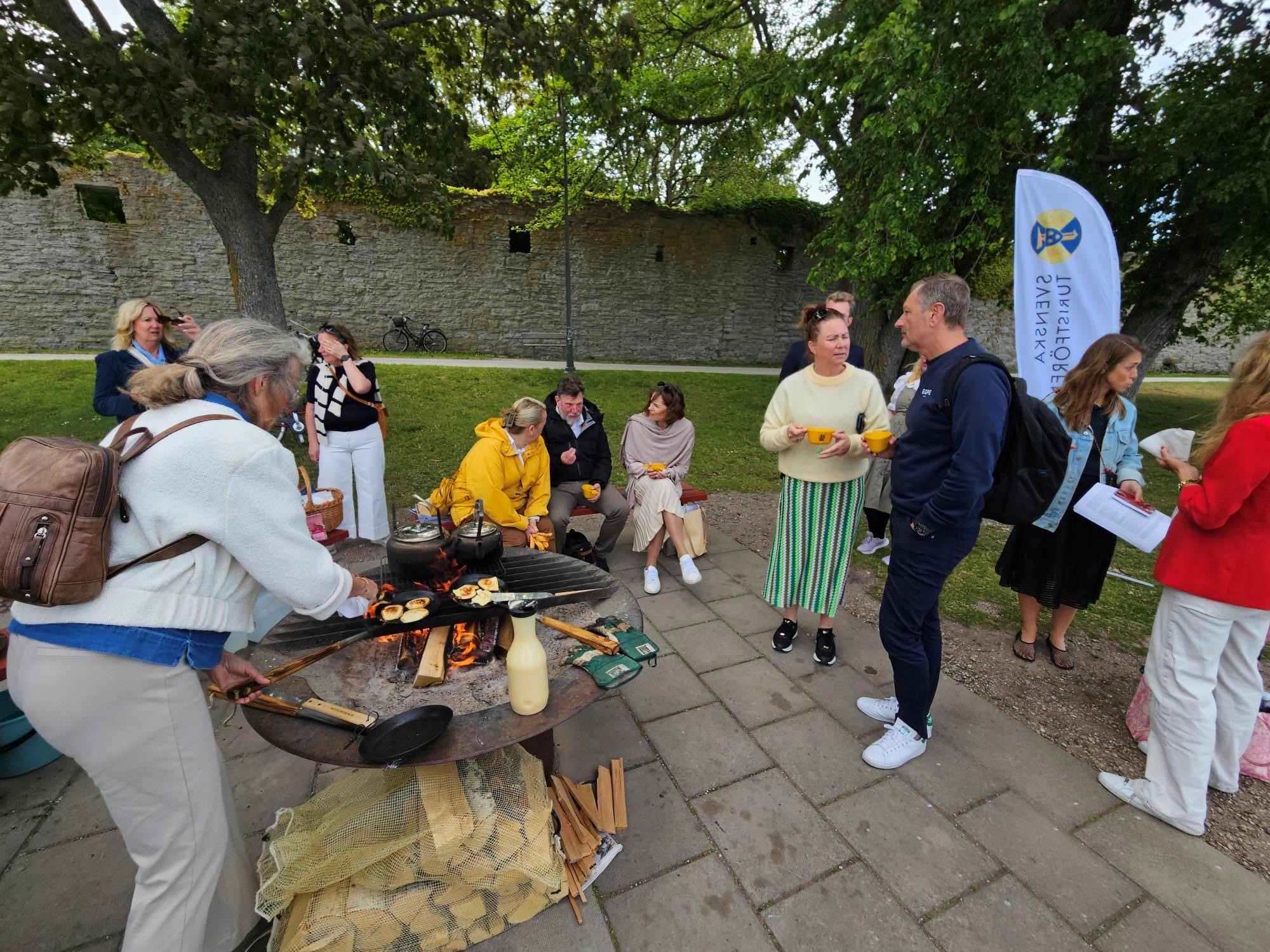 Personer runt en grillplats med tänd eld i Almedalen.