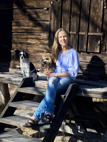 En kvinna sitter på en trapp till ett härbre i Tällberg tillsammans med två mindre hundar.