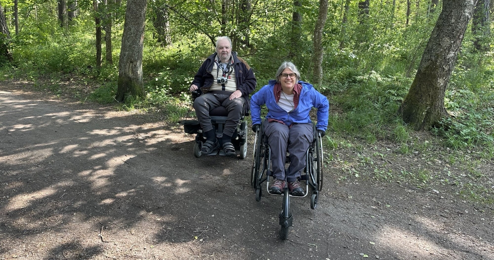 man och kvinna i rullstol i skogsområde på grusväg