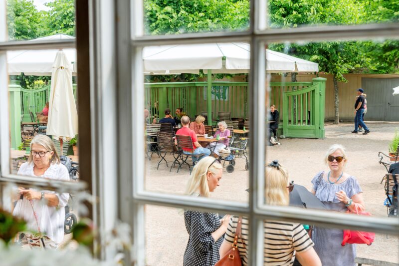 Besökare på en uteservering sett genom ett fönster från insidan på Gunnebo slott.