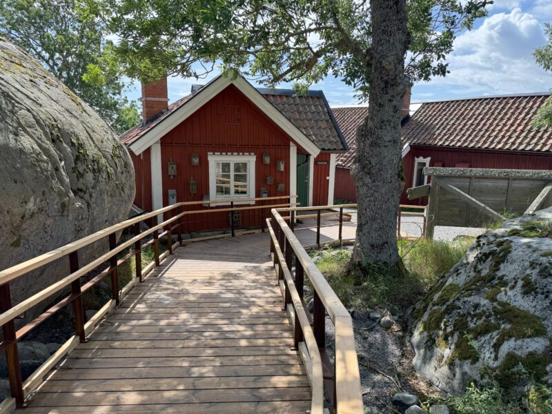 En tillgänglighetsanpassad träbro leder förbi ett rött hus i Nämdöfjärdens nationalpark.