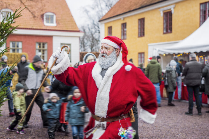 En rödklädd tomte på ett torg utomhus under en julmarknad.
