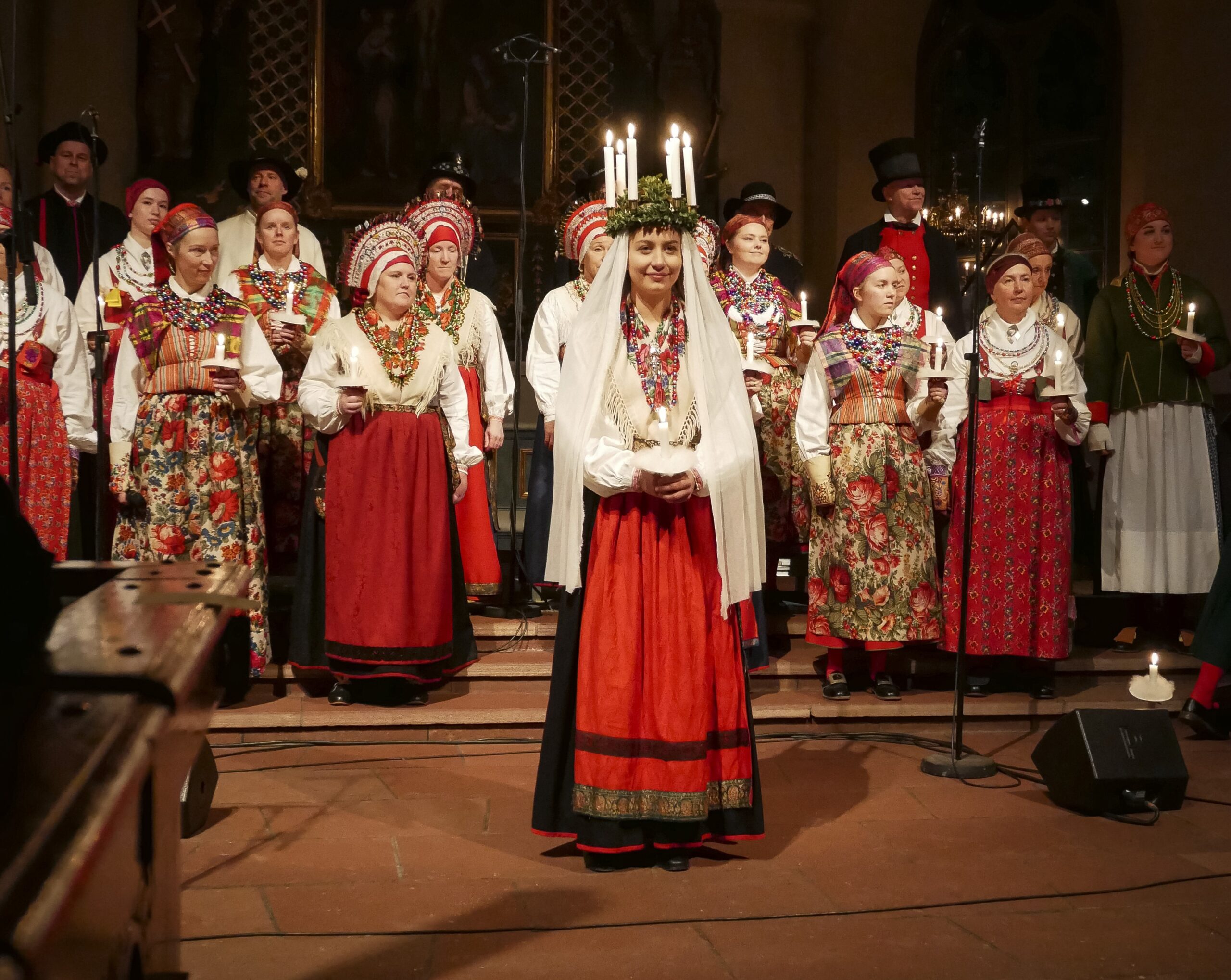 Lussibrud i vit särk, svart kjol och rött förkläde.