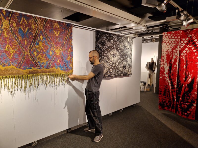 En man inspekterar en knuten matta i en konsthall.