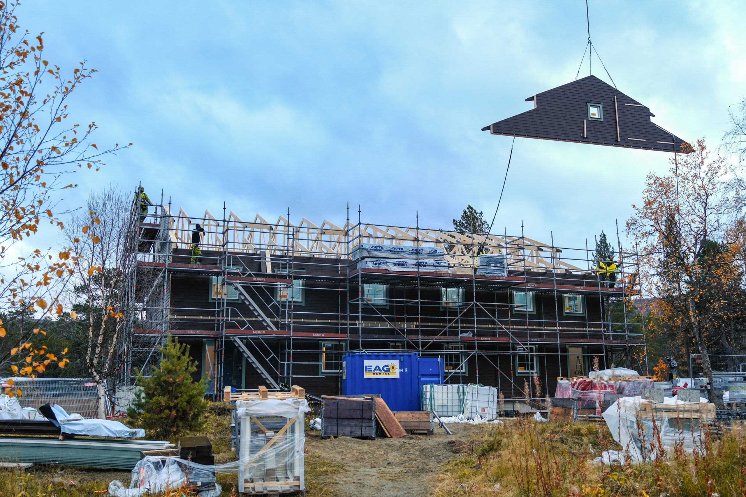 En takdel lyfts på plats med helikopter på ett hus omgivet av byggnadsställningar i Saltoluokta