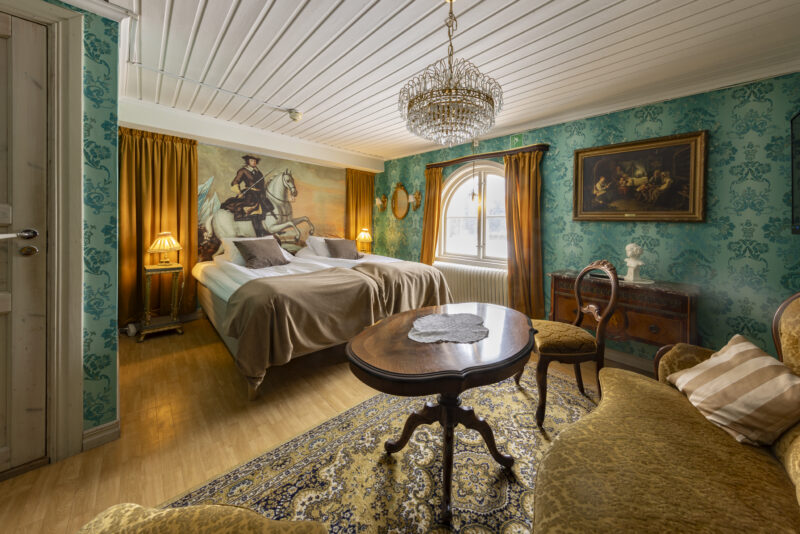 Ett sovrum inrett i äldre stil med medaljongtapeter och kristallkrona.