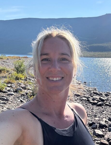 Selfie på person i svart bikini med en sjö och ett fjäll i bakgrunden.