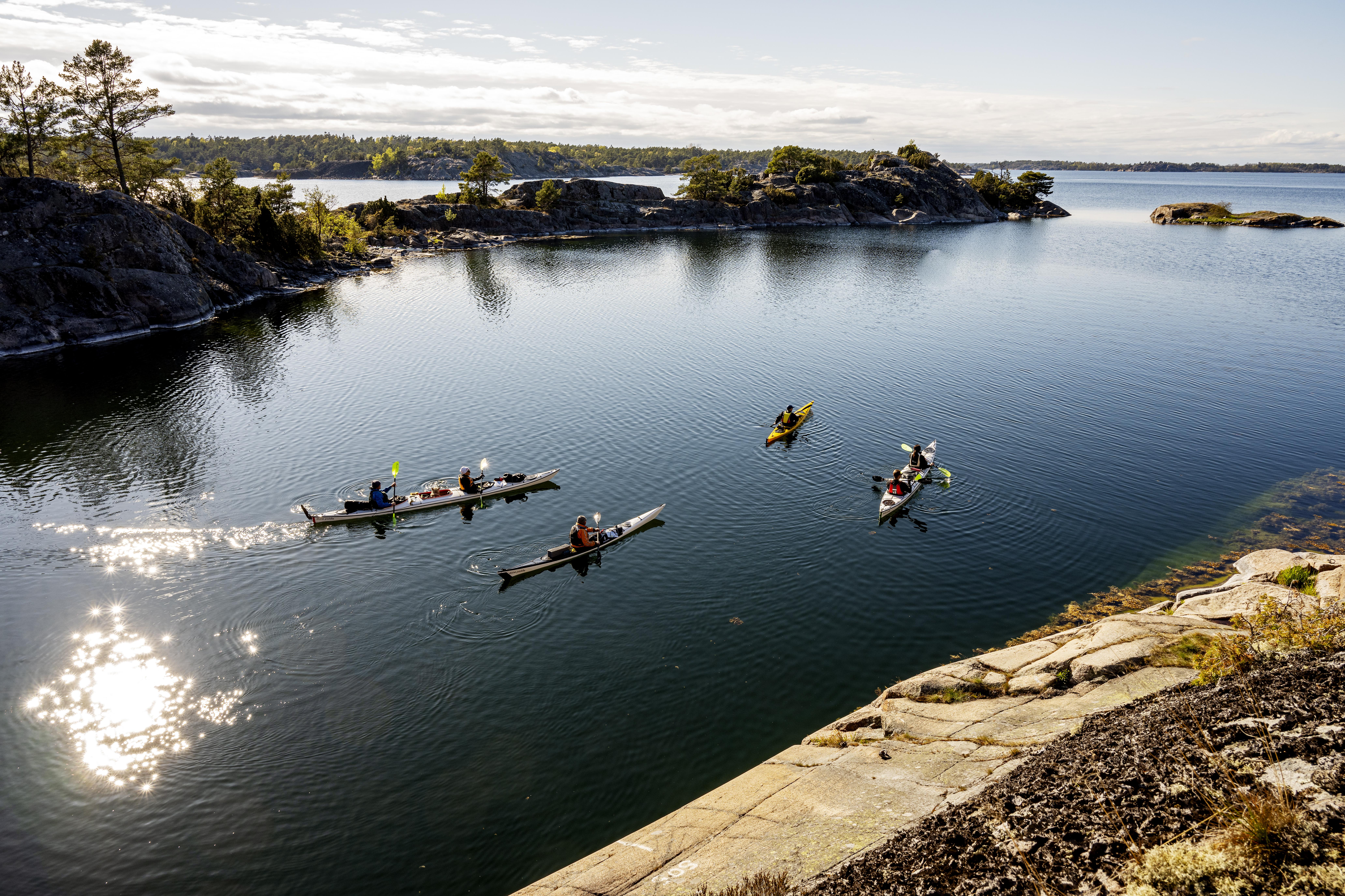 Fyra kajaker på spegelblankt vatten. Bilden tagen uppifrån en klippa.