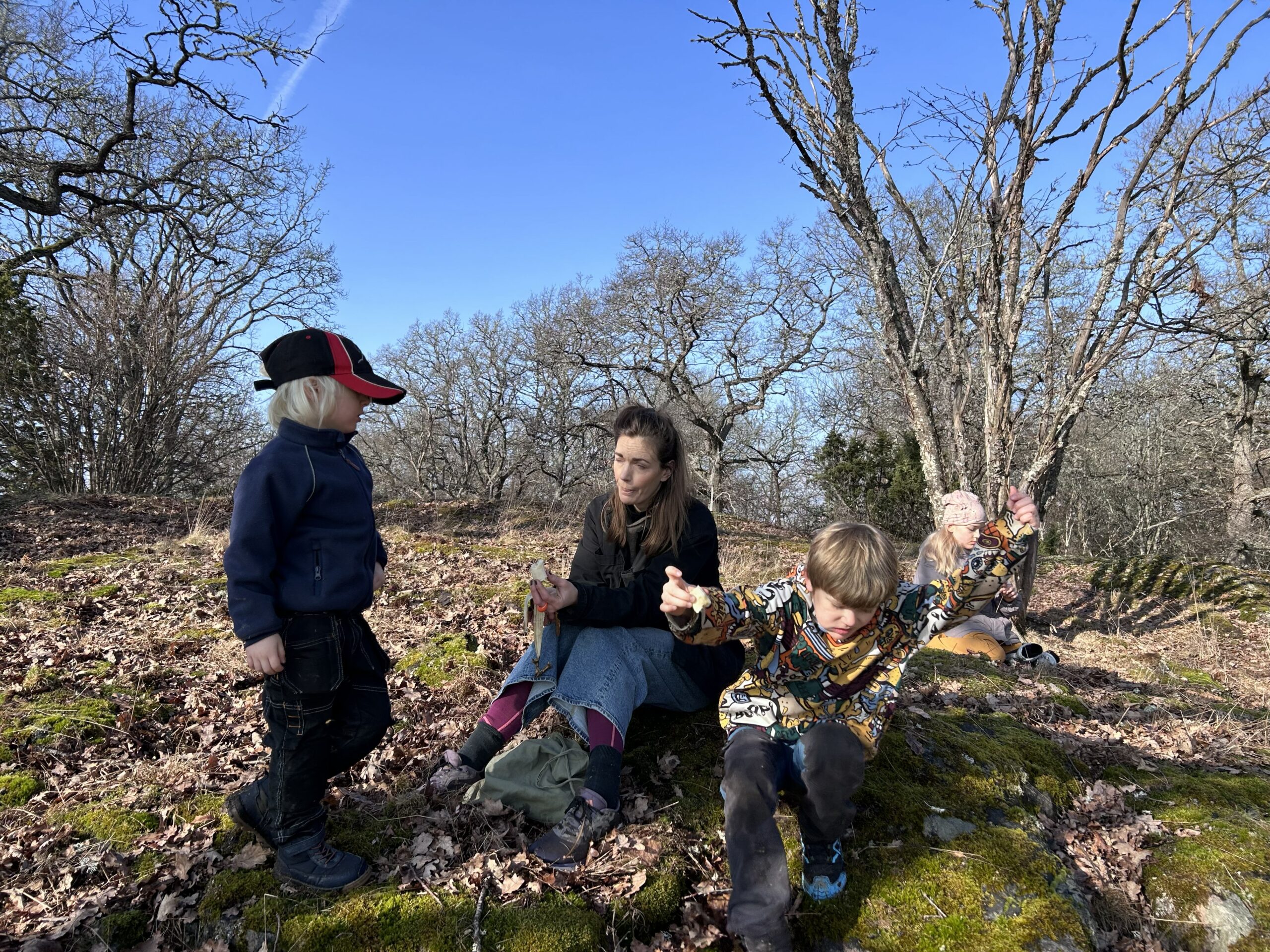 Familj byter skärm mot skärm. En kvinna med tre barn i en skogsbacke på våren.
