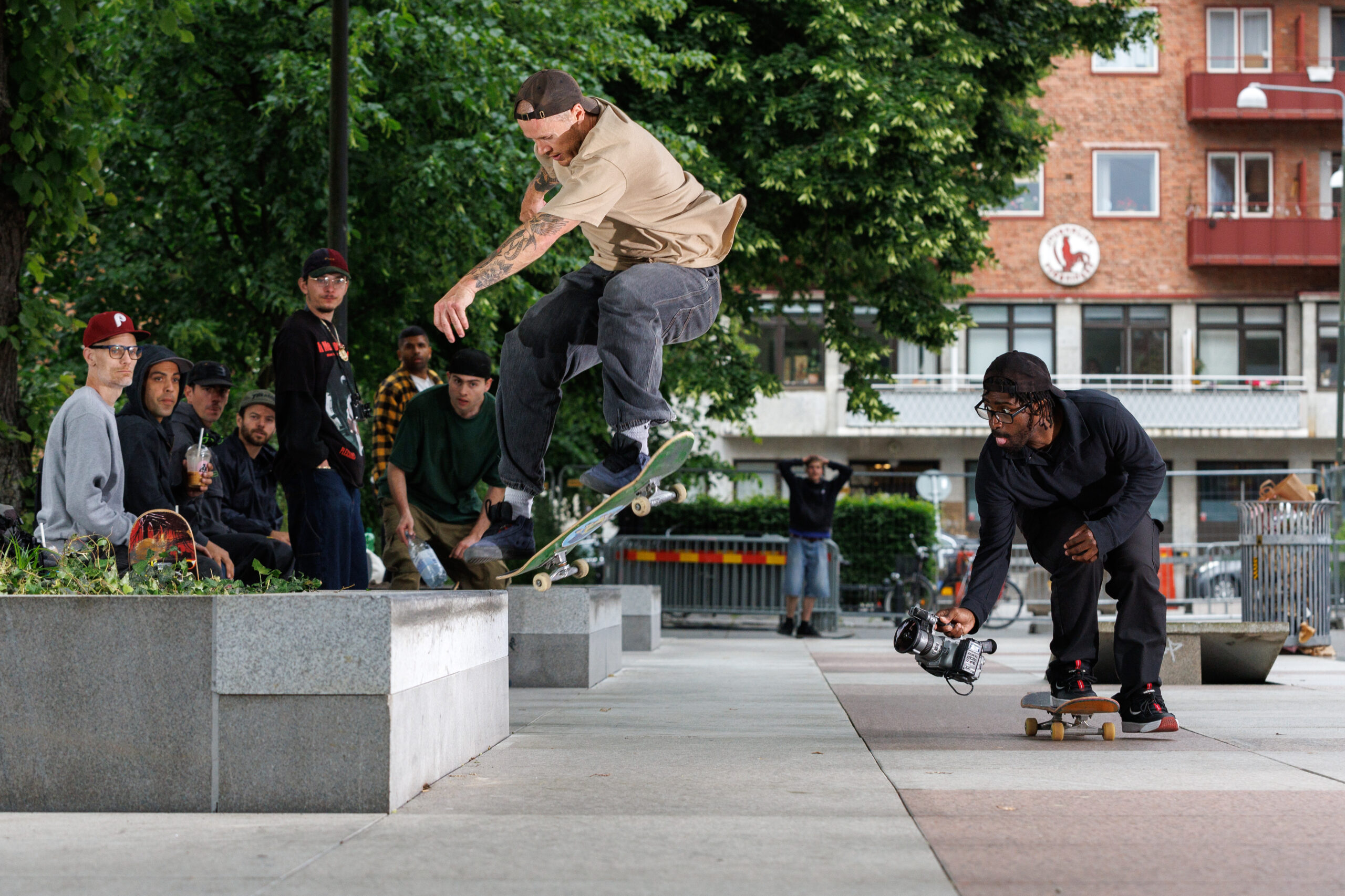 En man gör ett trick på en skateboard medan flera andra tittar på och en person filmar i parken Love Malmö.