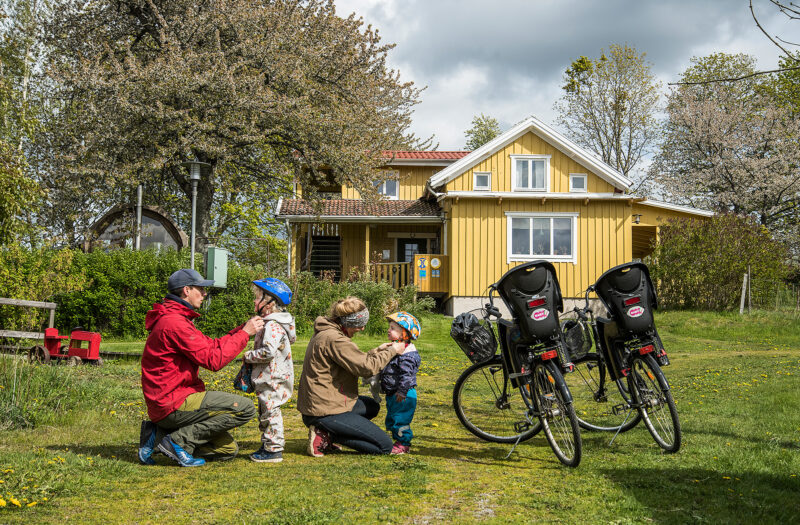 En familj förbereder sig för en cykeltur med Lugnåsbergets gula villa i bakgrunden.