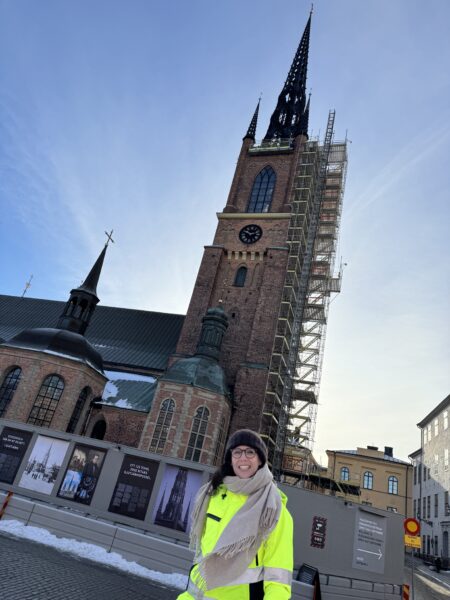 Kvinna i gula varselkläder framför Riddarholmskyrkan i Stockholm.