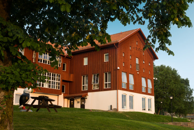 En röd stalliknande byggnad på Nordens Ark med grönskande löv i förgrunden.