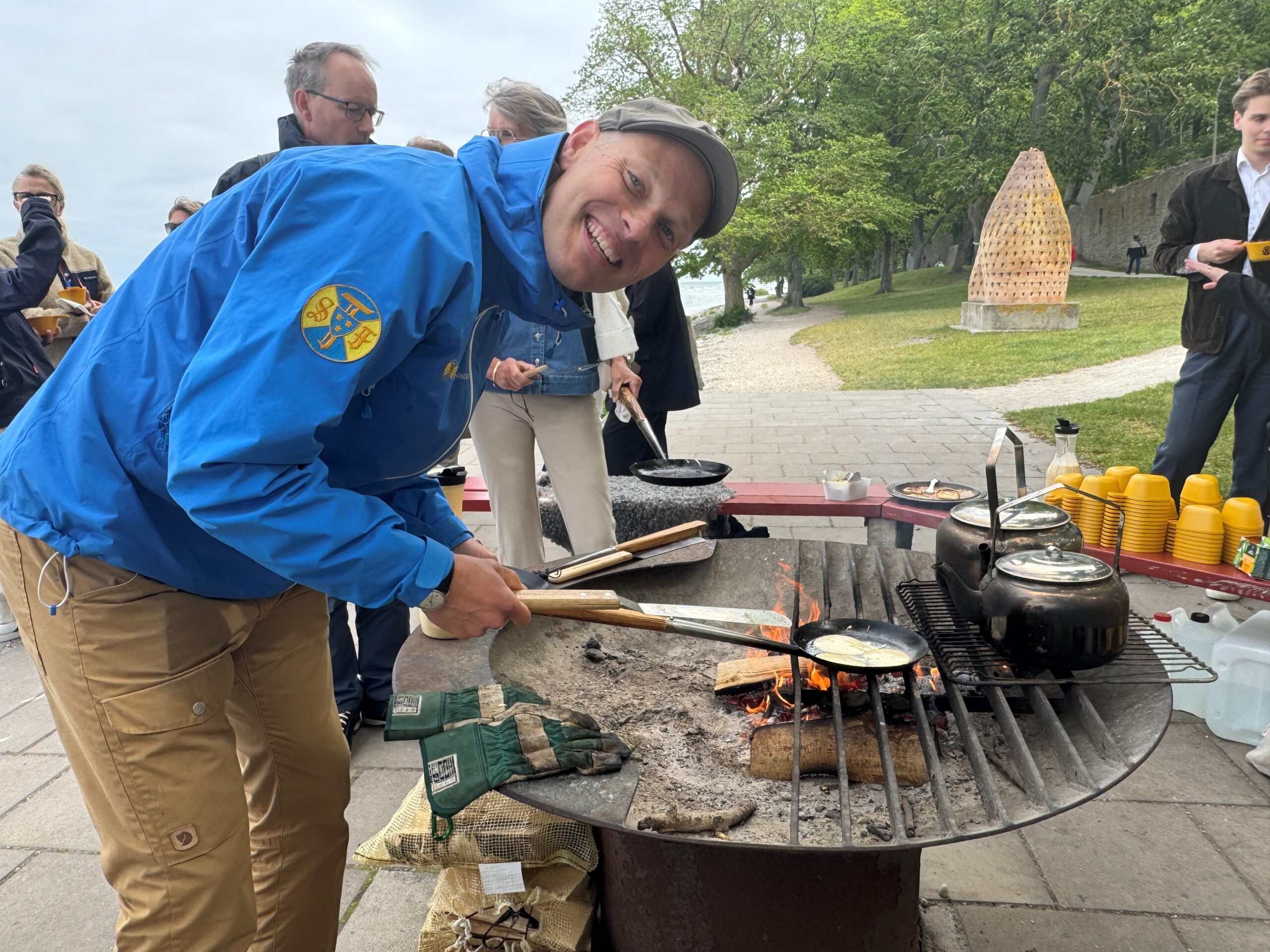 En man i blå jacka och gubbkeps steker krabbelurer på en grillhäll utanför ringmuren i Visby.