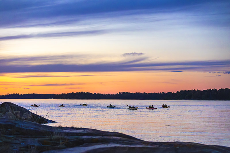 Rad med kajaker paddlar i skärgårdsmiljö i solnedgång