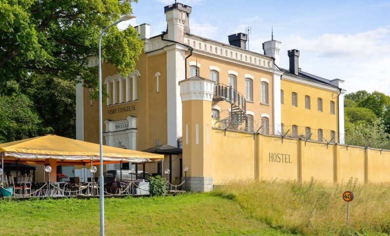 Visby fängelse, en gulputsad byggnad med gulputsad mur framför samt ett café under skärmtak.
