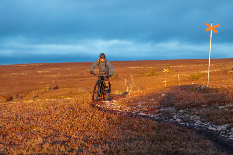 En cyklist på en stenig fjällstig på kalfjället i orange eftermiddagsljus.