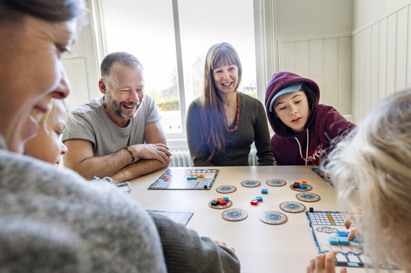 Vuxna och barn runt ett bord med sällskapsspel under en analog retreat.