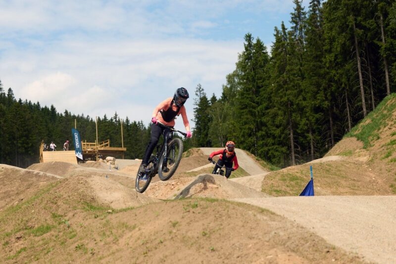 Två cyklister kör en så kallad pumptrack, en sandig bana med gupp där de hoppar med cyklarna.